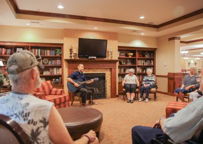 people sitting in a room listening to a man play the guitar